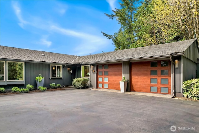 single story home with an attached garage, aphalt driveway, and roof with shingles