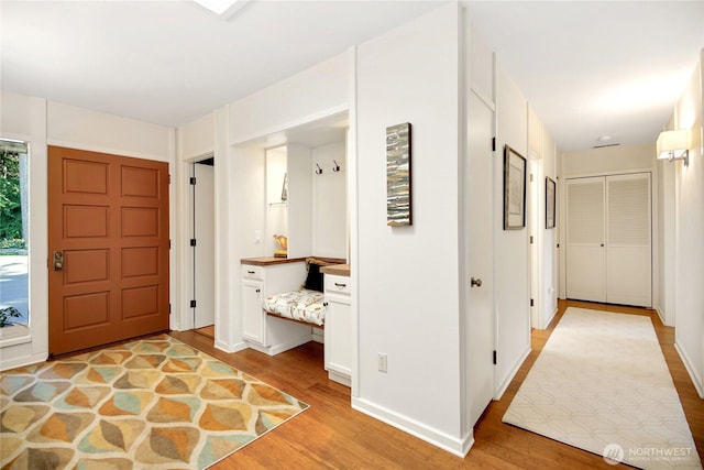 entrance foyer with baseboards, light wood finished floors, and built in desk