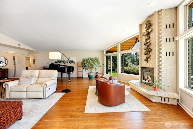 living area featuring lofted ceiling, baseboards, wood finished floors, and a brick fireplace