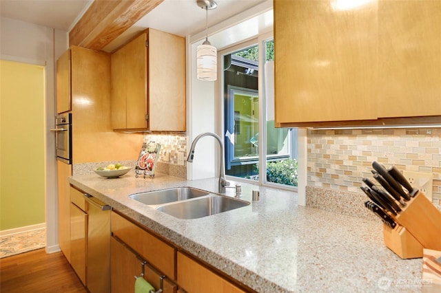 kitchen with wood finished floors, a sink, stainless steel oven, pendant lighting, and backsplash