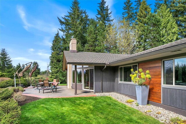 back of property with a patio area, a shingled roof, a chimney, and a yard