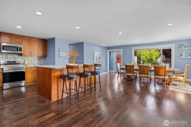 kitchen featuring baseboards, a kitchen island, brown cabinets, and appliances with stainless steel finishes