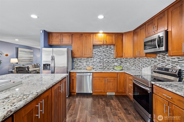 kitchen with stainless steel appliances, a sink, dark wood finished floors, light stone counters, and brown cabinetry