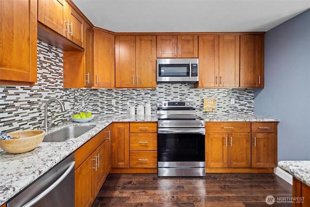 kitchen featuring dark wood-style floors, a sink, light stone counters, brown cabinetry, and appliances with stainless steel finishes
