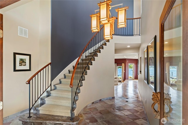 entryway featuring stairway, a towering ceiling, stone tile flooring, and visible vents