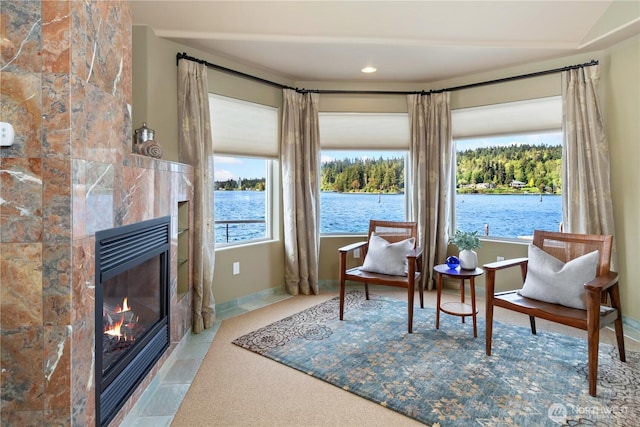 living area with a tiled fireplace, carpet, a water view, and baseboards