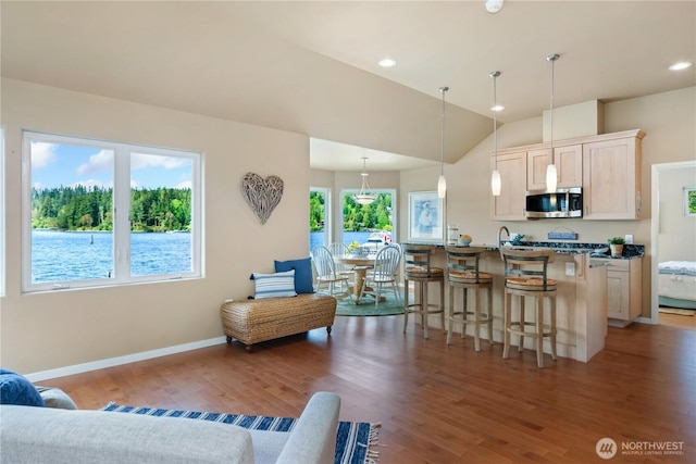 kitchen with decorative light fixtures, stainless steel microwave, wood finished floors, and a kitchen bar
