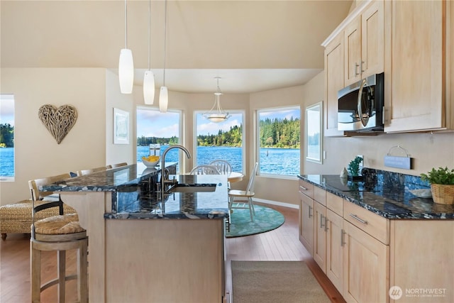 kitchen featuring light brown cabinetry, a sink, a breakfast bar area, stainless steel microwave, and wood finished floors