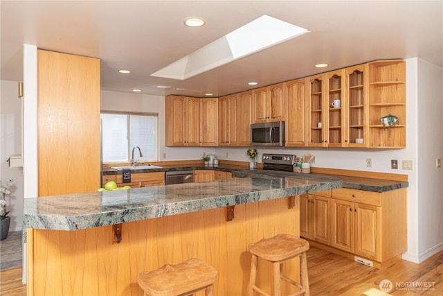 kitchen featuring appliances with stainless steel finishes, a sink, a kitchen breakfast bar, light wood-style flooring, and a skylight