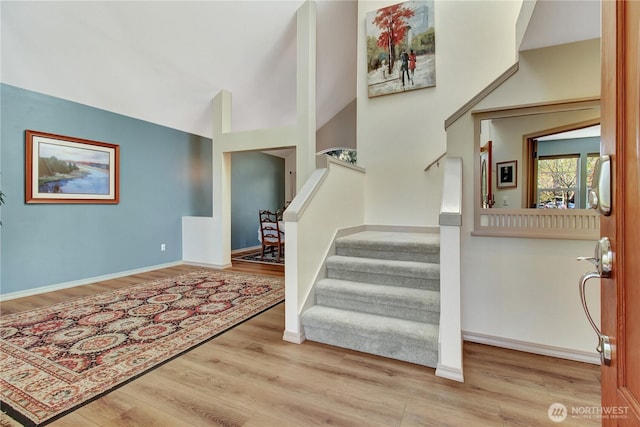 entryway with baseboards, vaulted ceiling, wood finished floors, and stairway