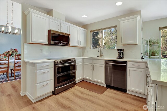 kitchen with a sink, light wood-style floors, stainless steel appliances, light countertops, and white cabinets
