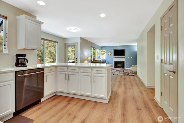kitchen featuring a glass covered fireplace, light wood-type flooring, dishwasher, white cabinets, and a peninsula