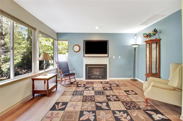 living area with baseboards, a glass covered fireplace, visible vents, and light wood-type flooring
