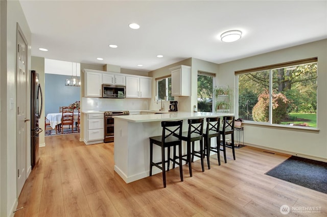 kitchen featuring light wood finished floors, stainless steel appliances, a sink, a peninsula, and a breakfast bar area