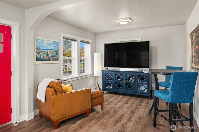 living area with arched walkways, baseboards, and wood finished floors
