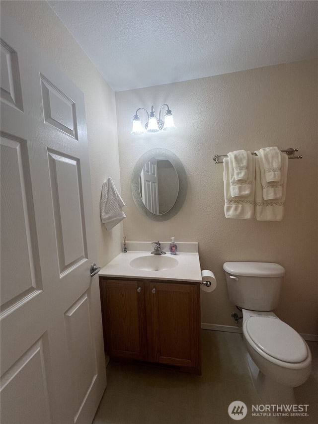 half bath with toilet, a textured ceiling, baseboards, and vanity