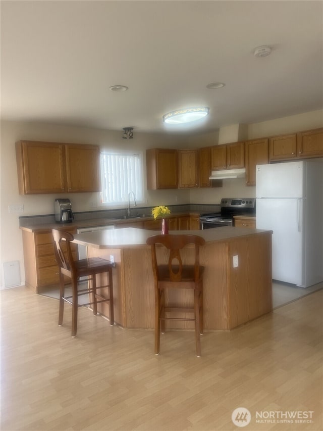 kitchen with stainless steel electric range oven, brown cabinetry, a center island, freestanding refrigerator, and under cabinet range hood