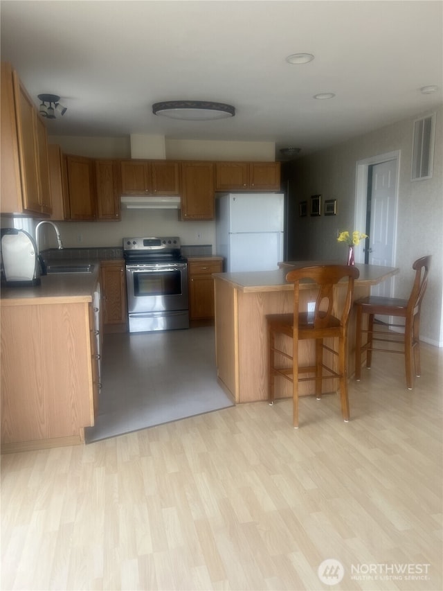 kitchen with visible vents, freestanding refrigerator, electric range, brown cabinetry, and a sink