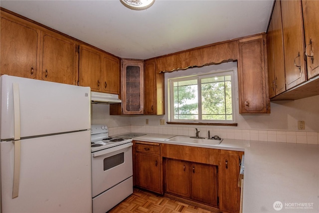 kitchen with a sink, white appliances, brown cabinets, light countertops, and under cabinet range hood