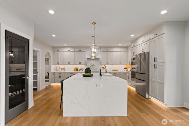 11016 46th St E, Edgewood, WA 98372 - kitchen featuring freestanding refrigerator, a sink, light wood finished floors, arched walkways, and light stone countertops
