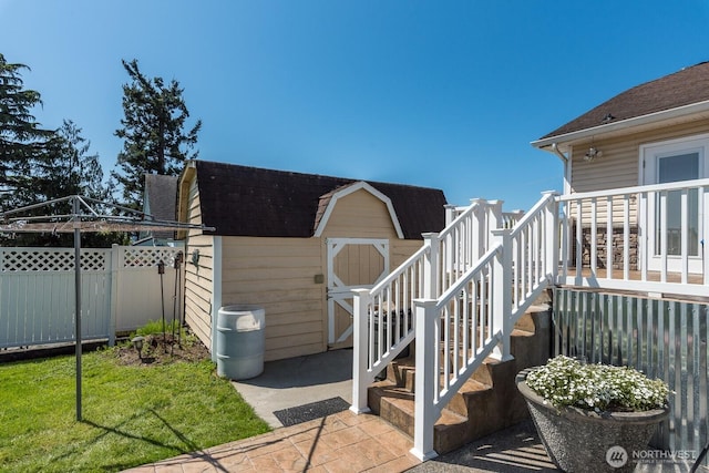 exterior space with fence, a shingled roof, an outdoor structure, and a storage unit