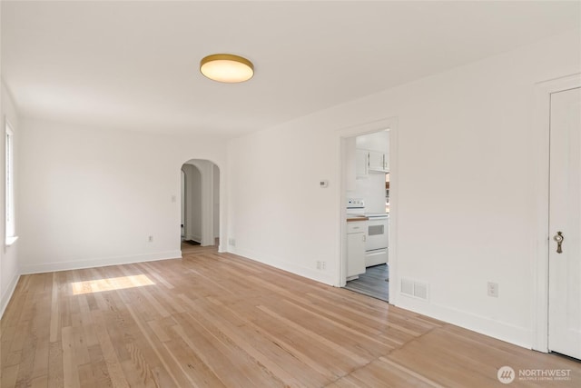 spare room with visible vents, baseboards, light wood-style flooring, and arched walkways