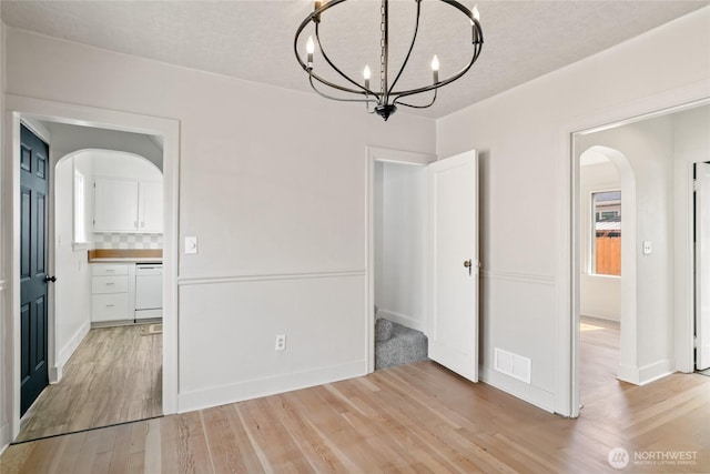 unfurnished dining area featuring light wood-style floors, a notable chandelier, visible vents, a textured ceiling, and arched walkways