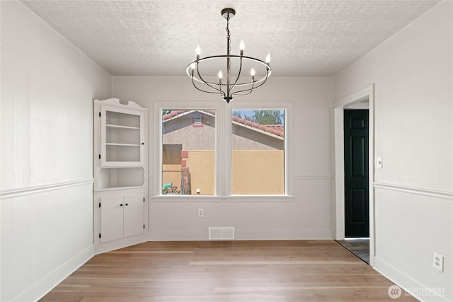 unfurnished dining area featuring light wood finished floors, a chandelier, visible vents, baseboards, and a textured ceiling