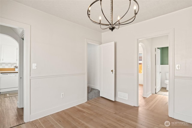 unfurnished dining area featuring visible vents, arched walkways, a notable chandelier, and light wood-style flooring