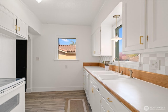 kitchen featuring white cabinets, a sink, light countertops, baseboards, and light wood finished floors