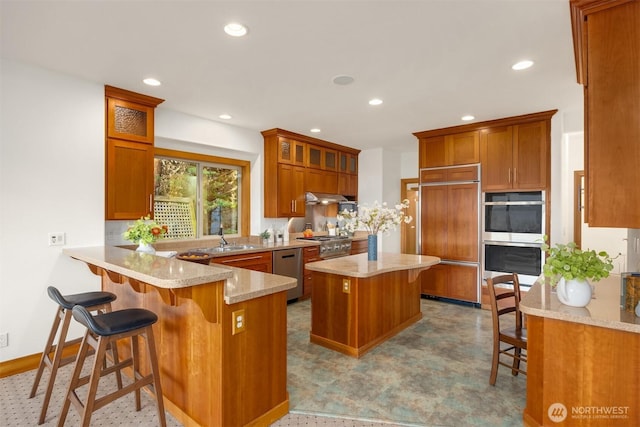 kitchen featuring stainless steel appliances, brown cabinetry, recessed lighting, a breakfast bar area, and glass insert cabinets