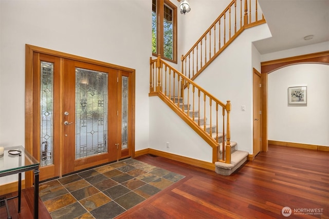 entrance foyer featuring a towering ceiling, baseboards, stairs, and wood finished floors