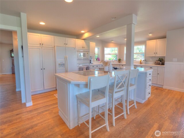 kitchen featuring light countertops, a center island, white cabinets, and white appliances