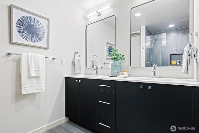 full bathroom with double vanity, baseboards, a stall shower, and a sink