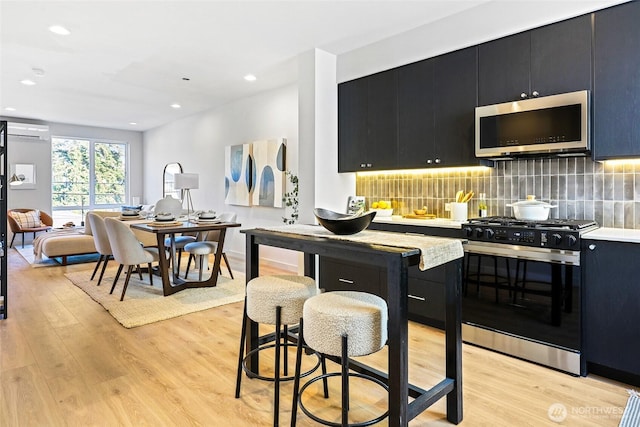 kitchen with stainless steel microwave, light wood-type flooring, range with gas cooktop, and dark cabinetry