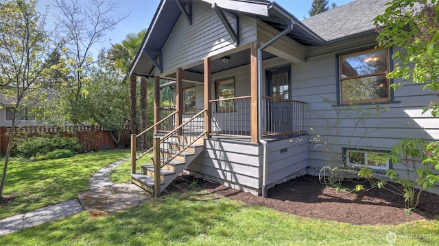 view of front of home featuring covered porch, a shingled roof, a front yard, and fence
