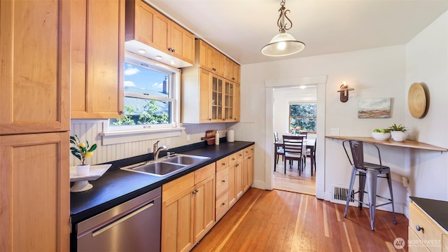 kitchen featuring light wood finished floors, a sink, dark countertops, dishwasher, and hanging light fixtures