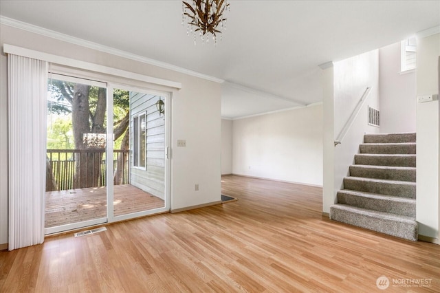 unfurnished living room featuring ornamental molding, a notable chandelier, stairway, and wood finished floors