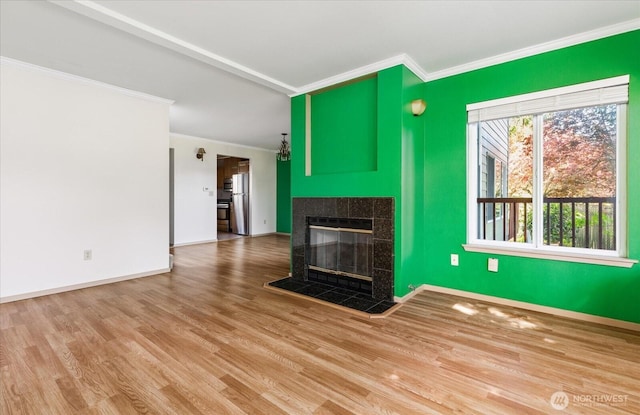 unfurnished living room with wood finished floors, a tiled fireplace, crown molding, and baseboards