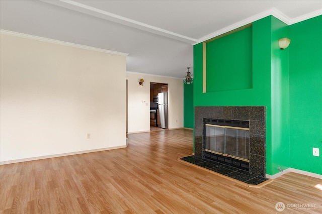 unfurnished living room with crown molding, a tiled fireplace, wood finished floors, and baseboards