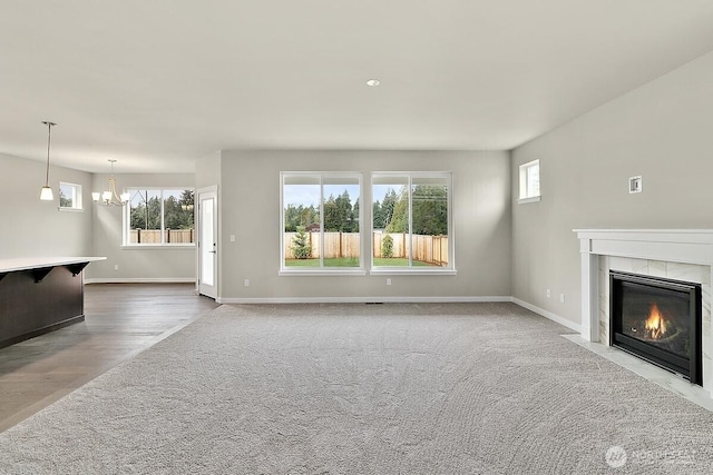 unfurnished living room with wood finished floors, a tiled fireplace, a notable chandelier, and baseboards
