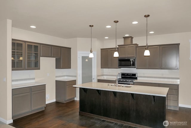 kitchen featuring dark wood finished floors, an island with sink, stainless steel appliances, light countertops, and baseboards