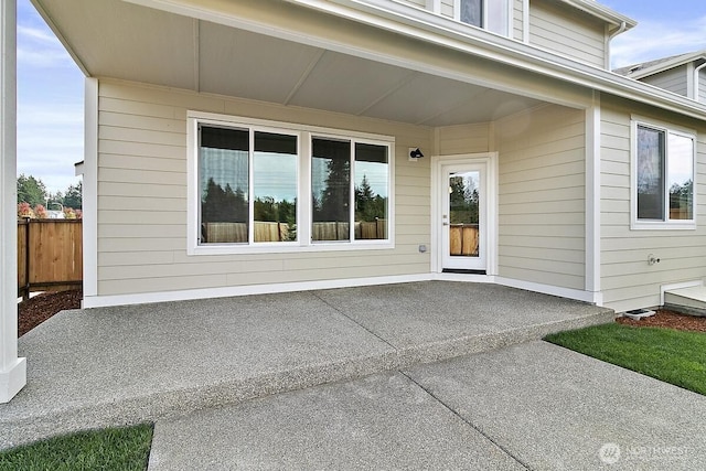 view of exterior entry featuring a patio and fence