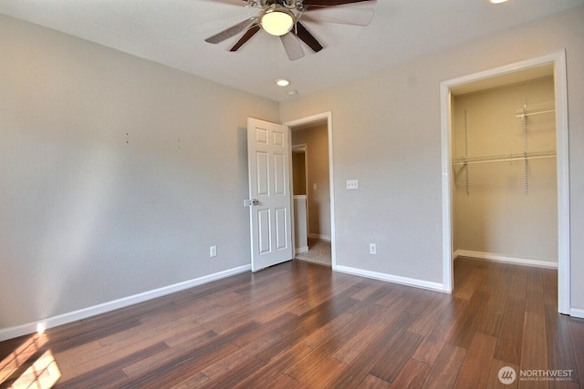 unfurnished bedroom featuring a spacious closet, wood finished floors, a ceiling fan, a closet, and baseboards