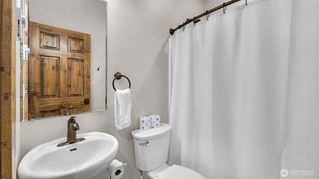 bathroom featuring toilet, curtained shower, and a sink