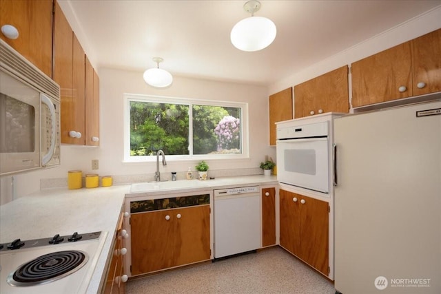 kitchen with white appliances, a sink, light countertops, and brown cabinets