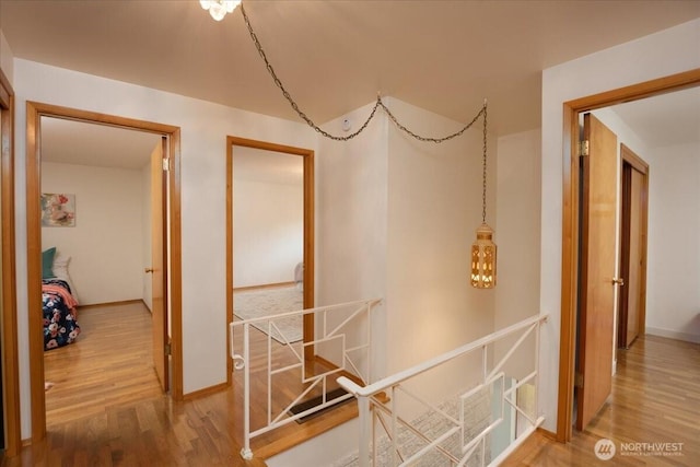 hallway with wood finished floors, baseboards, and an upstairs landing