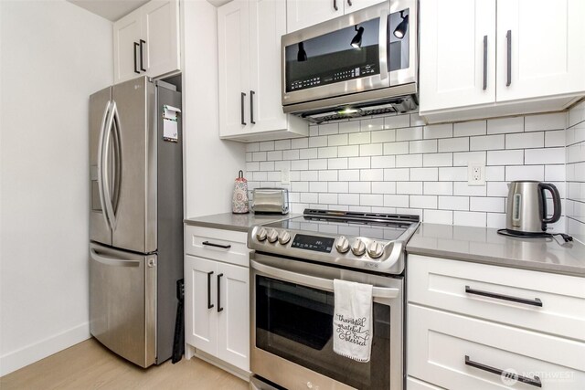 kitchen featuring baseboards, white cabinets, tasteful backsplash, light wood finished floors, and stainless steel appliances