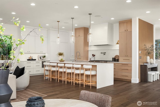 kitchen featuring dark wood-style floors, a kitchen bar, a center island with sink, premium range hood, and light countertops