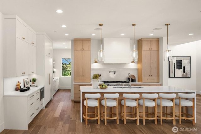 kitchen with wood finished floors, a sink, light countertops, a kitchen breakfast bar, and recessed lighting